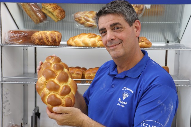 Man in blue shirt holding loaf of challah bread 