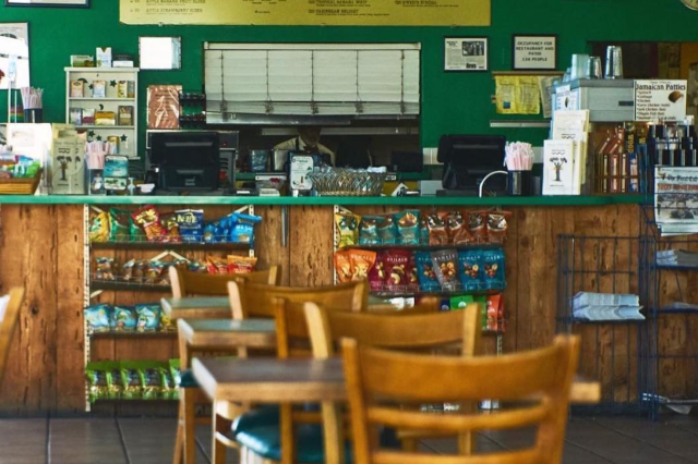 A restaurant with a green wall and yellow menu posted on the wall sits behind some restaurant tables and chairs