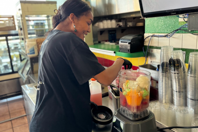Mia Keeling operating a commercial blender, watching as the ingredients for the signature "Yes We Can" smoothie mix together.