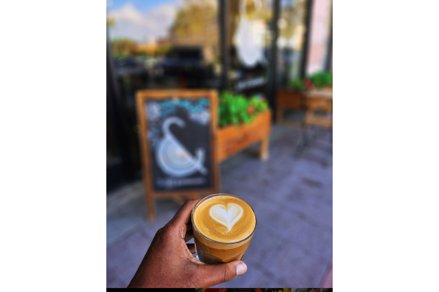 A small glass cup hold a latte drink with a heart drawn in the foam