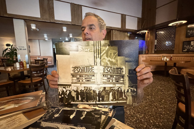 Man holding up a black and white 1950s photo of the Esquire Theatre marquee sign.