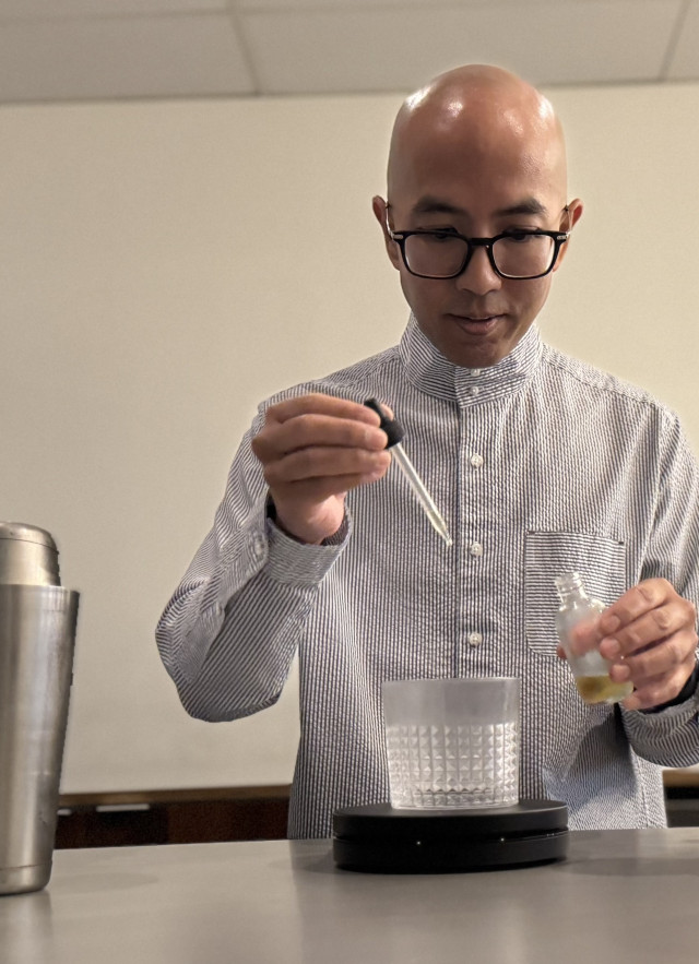 Bald man in glasses using a pipette to measure ingredients into a custom coffee drink.