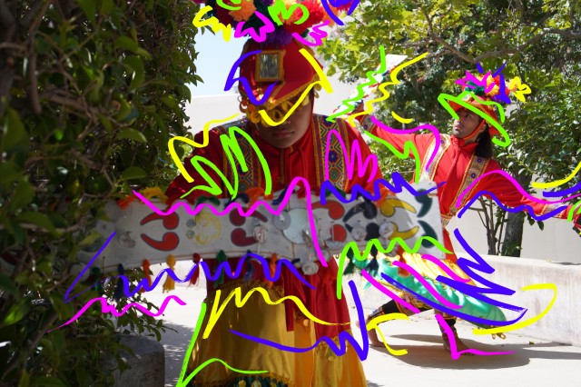 Two dancers wearing red headpieces and clothing with yellow, green, and purple squiggly shapes over them