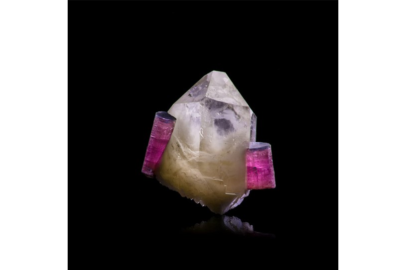 Clear rocket-shaped mineral with pink cylindrical crystal attached on the sides