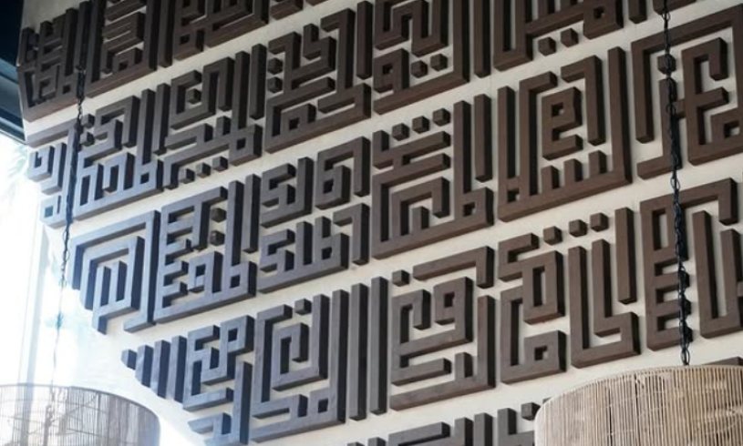 A prominent wall behind the cafe counter adorned with beautiful Arabic calligraphy displaying the 99 names of God